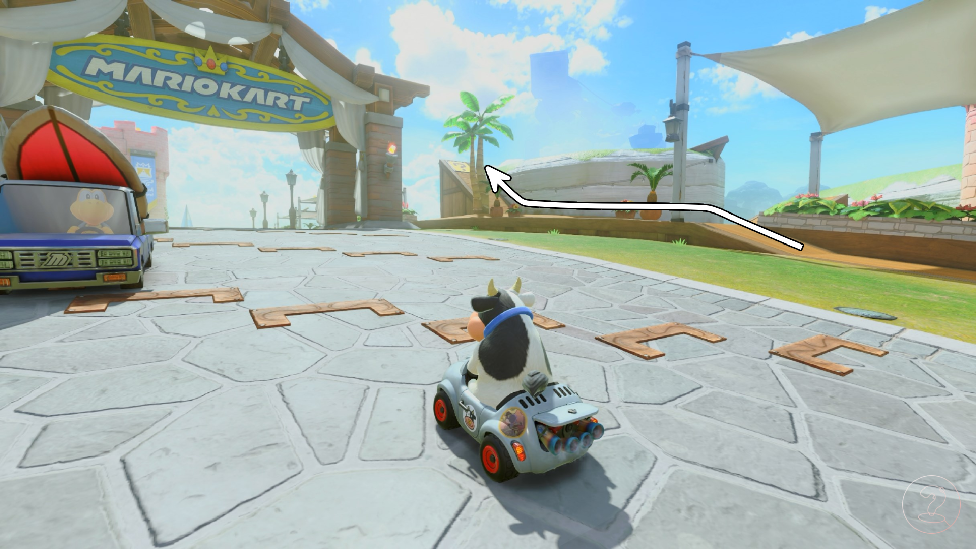 A cow sitting in a car on top of a stone road and palm trees in the background in Mario Kart World.
